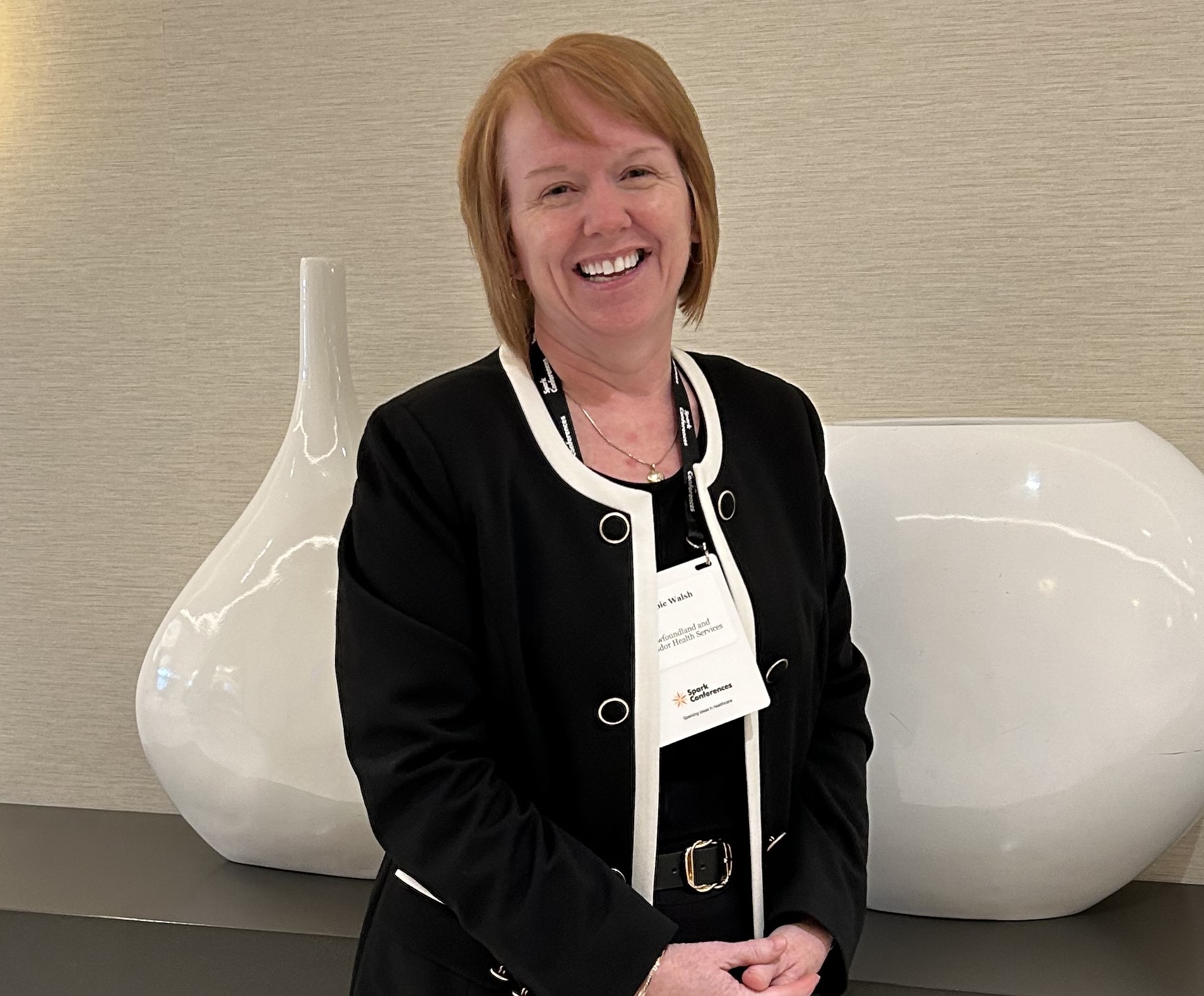 Debbie Walsh at the conference smiling for photo with decorative, white vases behind her