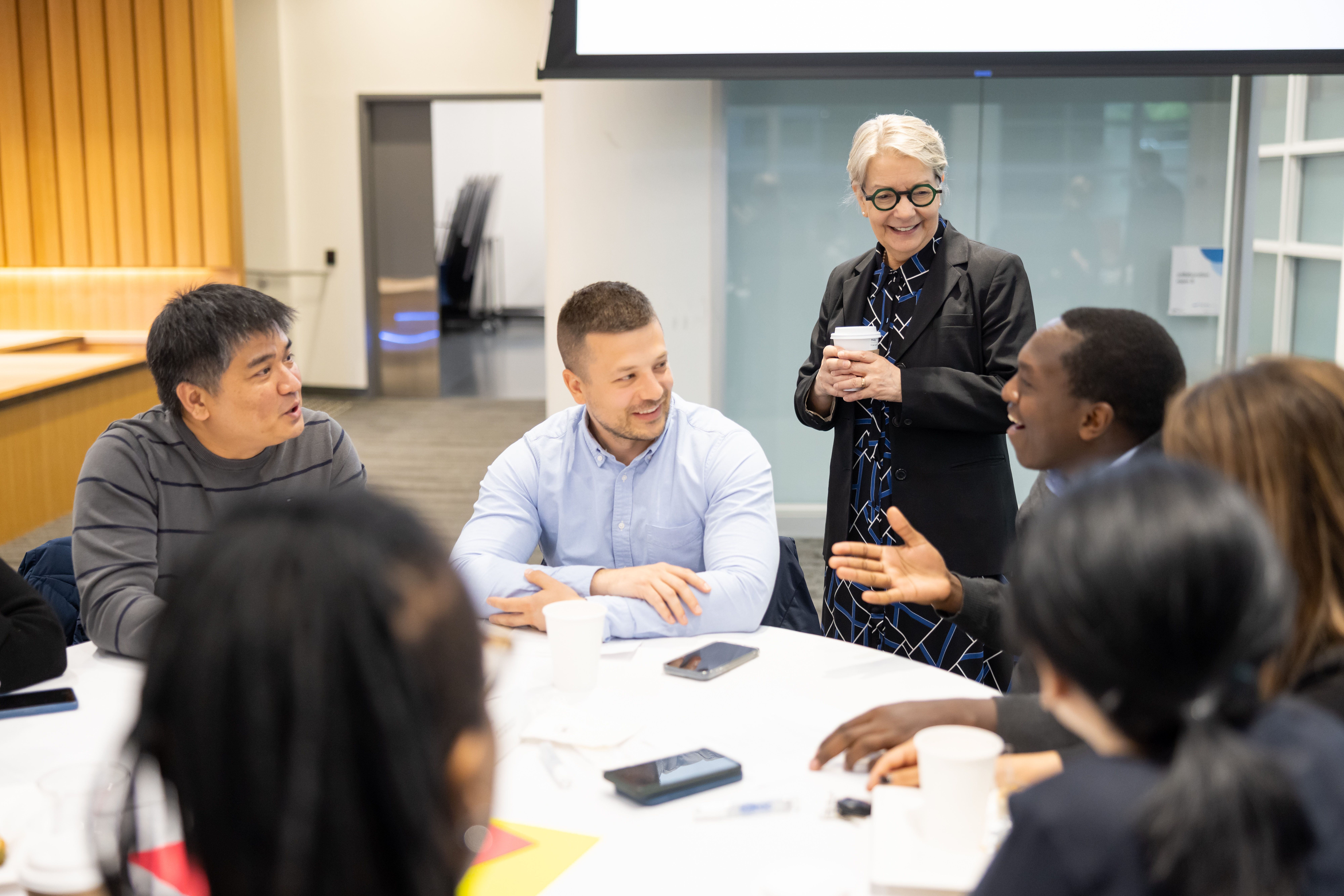 Catherine talks to a group of staff who are sitting around a table.