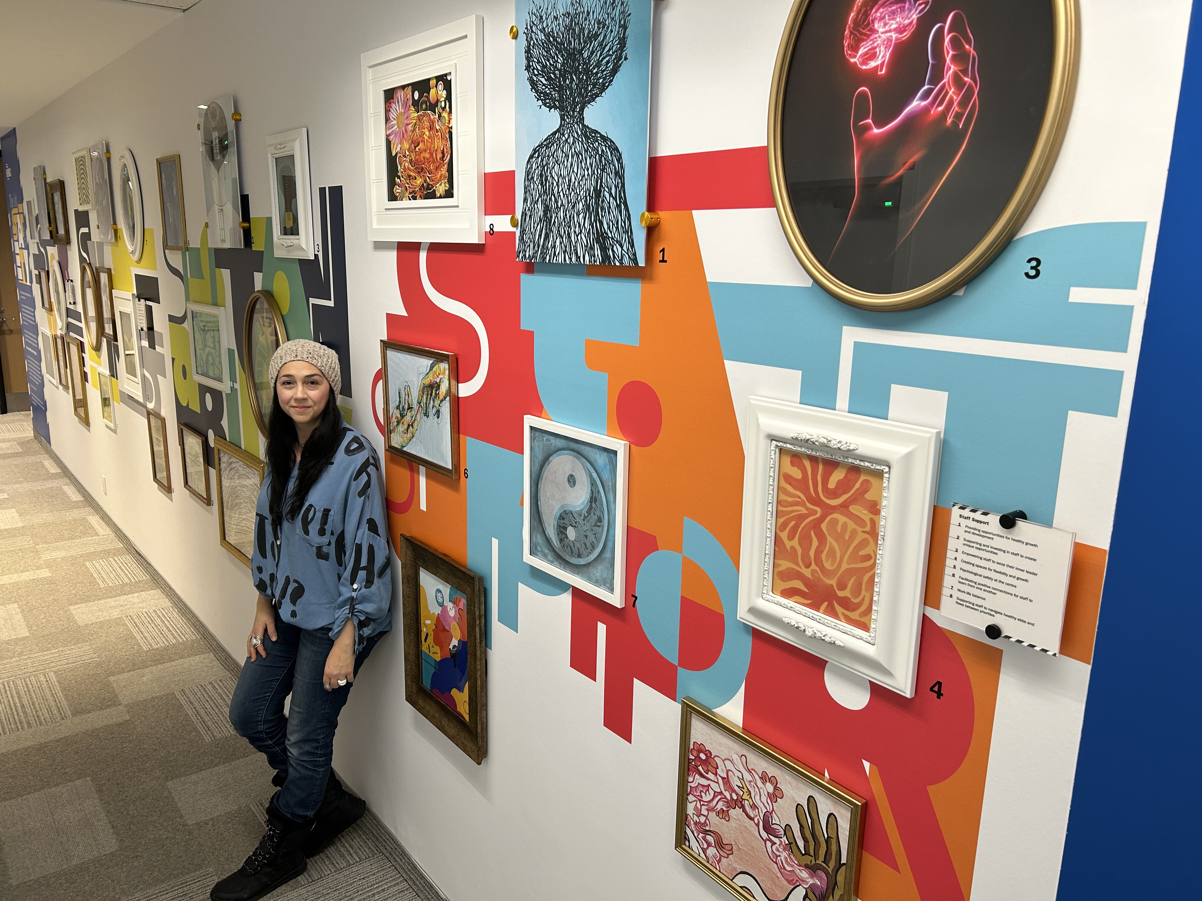 Graphic Designer Tania Volpe standing in front of the HIROC gallery wall