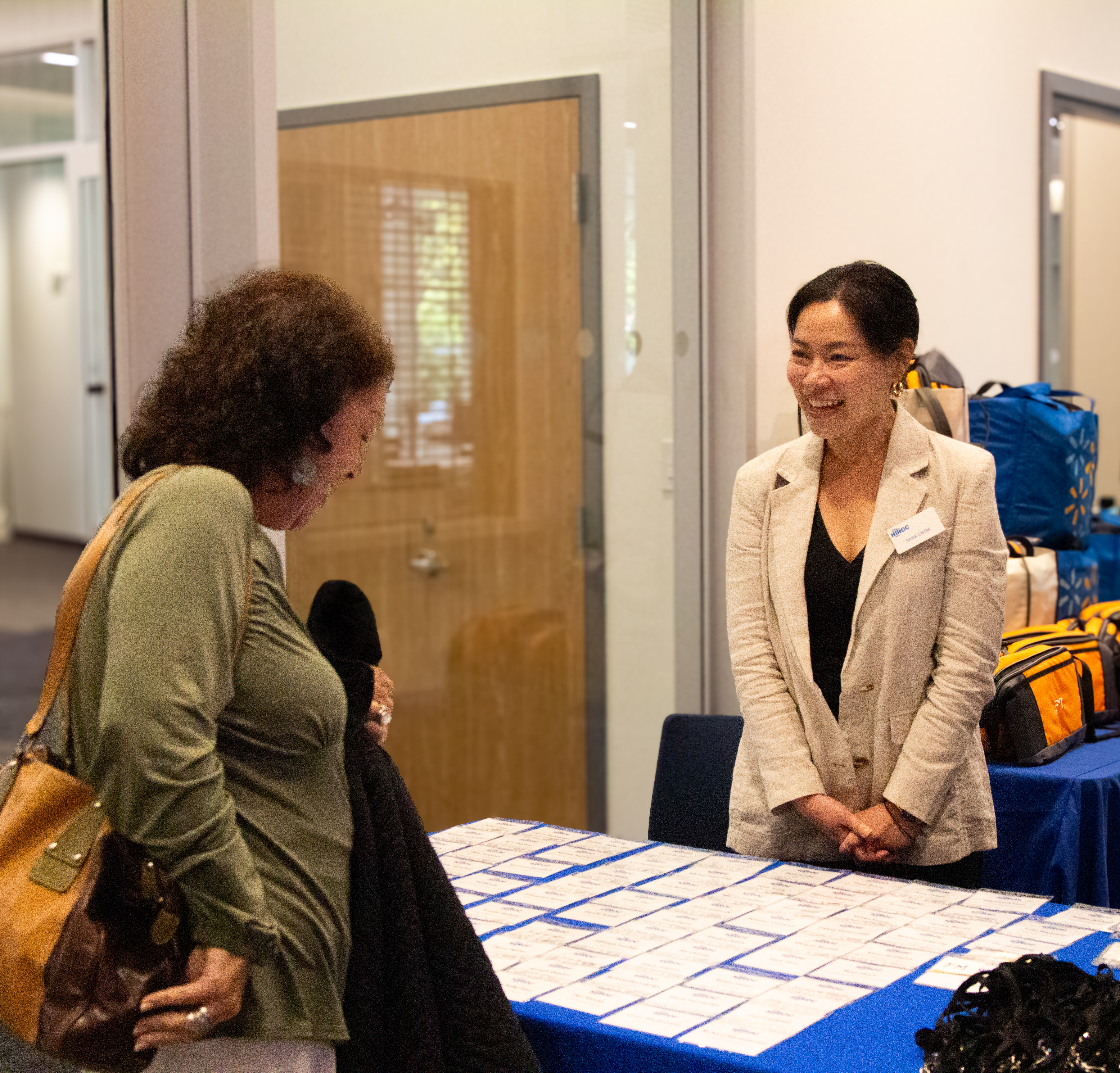 HIROC's Sara Chow, right, stands behind a table and greets an attendee.