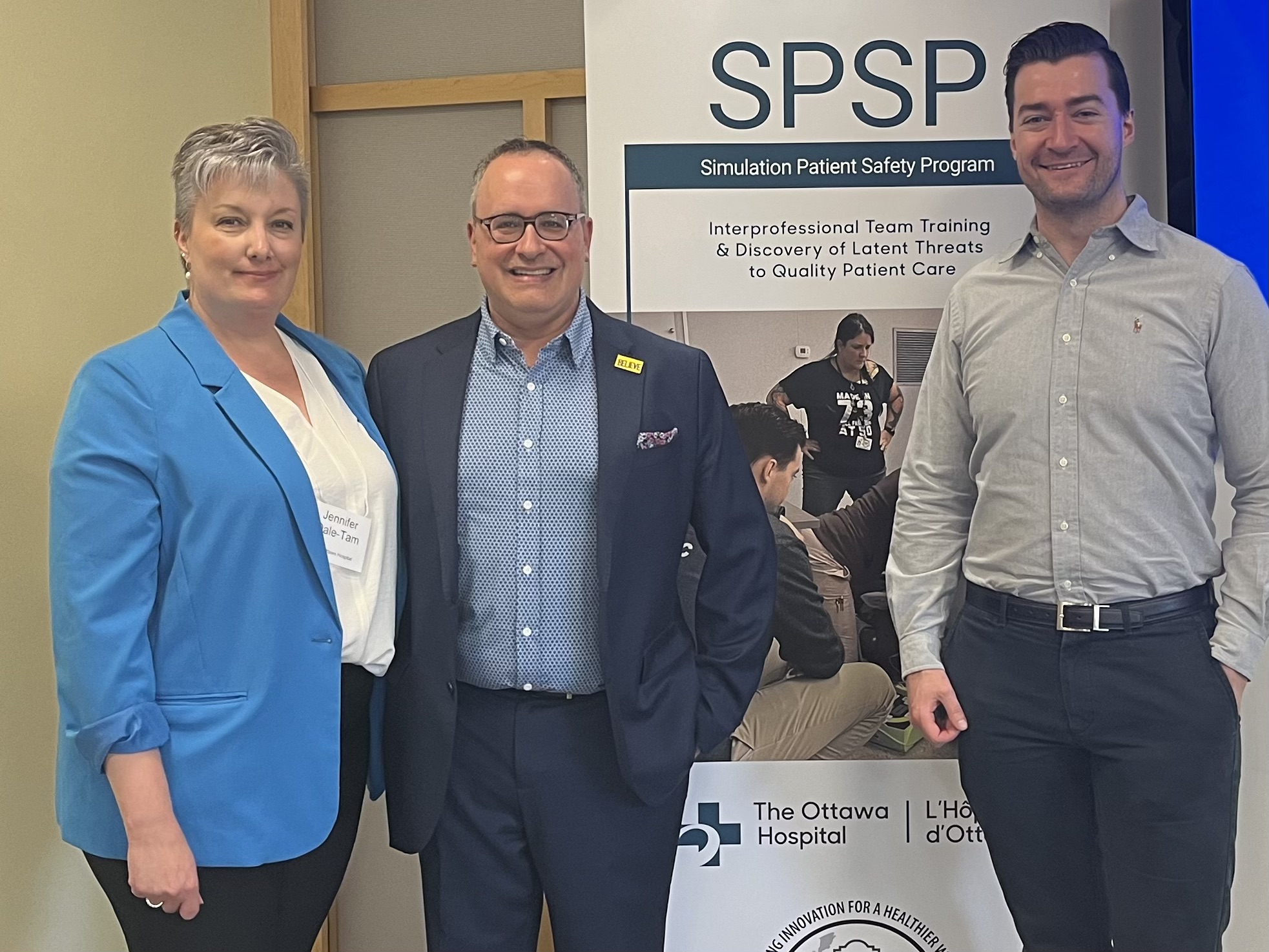 Jennifer Dale-Tam, Dr. Glenn Posner, and Dr. Doran Drew of TOH's Simulation Patient Safety Program stand and smile at the camera next to a poster for the program.
