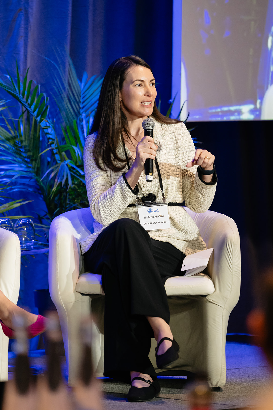Melanie de Wit sitting in a chair and holding a microphone while speaking on stage.