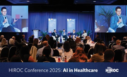 Wide shot of the HIROC Conference showing the AI panel speakers on stage and the audience sitting in front of them with the article title at the bottom.