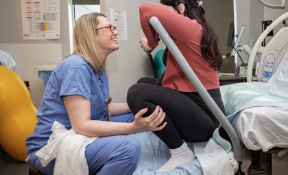 IWK's nurse sits on a hospital bed with a pregnant person, helping her with breathing.