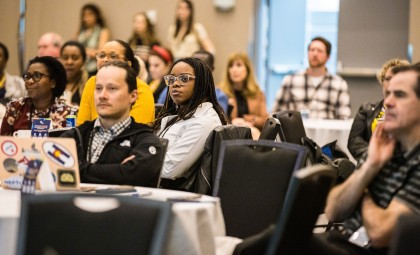 Attendees sit at tables to watch a presentation at Journées Montfort.