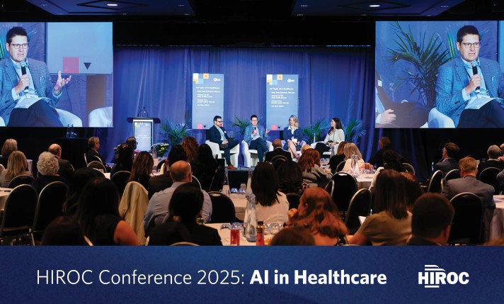 Wide shot of the HIROC Conference showing the AI panel speakers on stage and the audience sitting in front of them with the article title at the bottom.