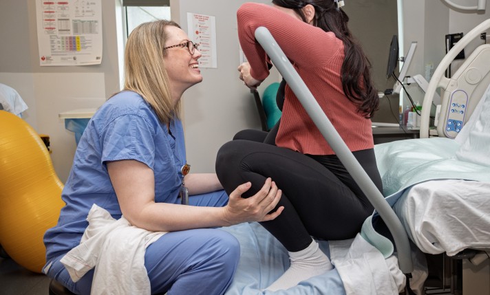 IWK's nurse sits on a hospital bed with a pregnant person, helping her with breathing.