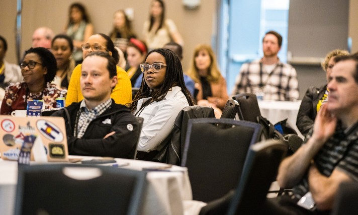 Attendees sit at tables to watch a presentation at Journées Montfort.