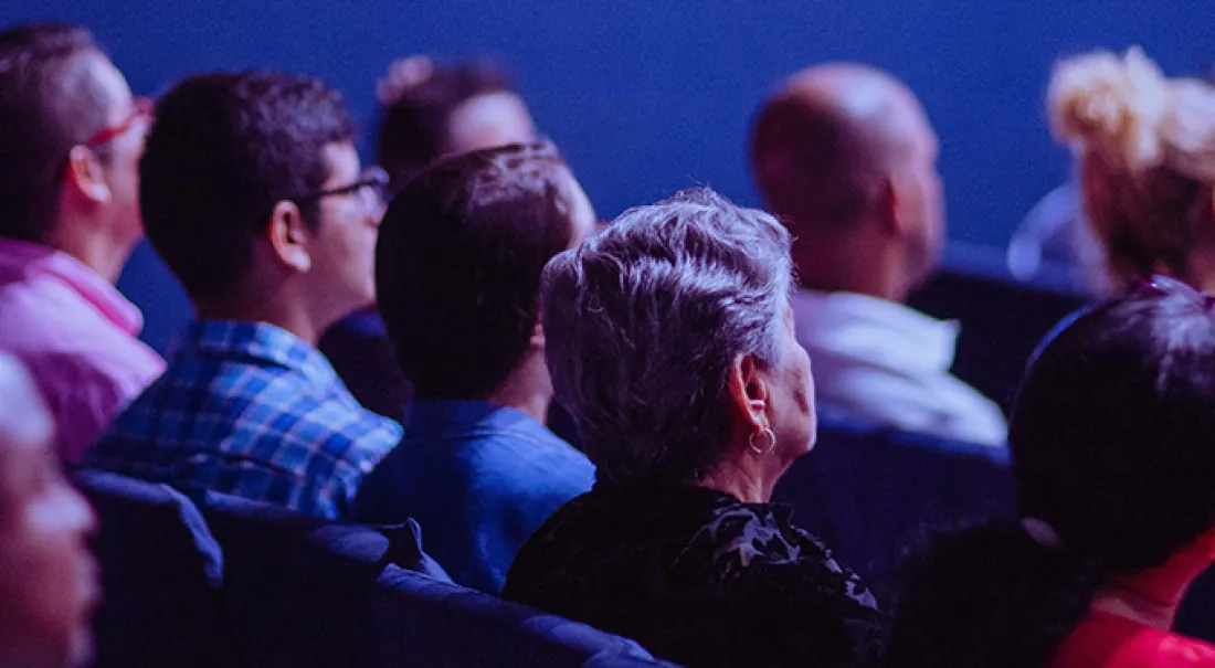 people sitting in a dimly lit room watching a conference session